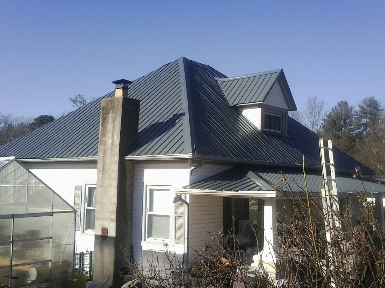 Dark blue standing seam metal roof on a white farmhouse with dormer — Slate & Tile Roof Repair by Roofing Brothers in Gurley
