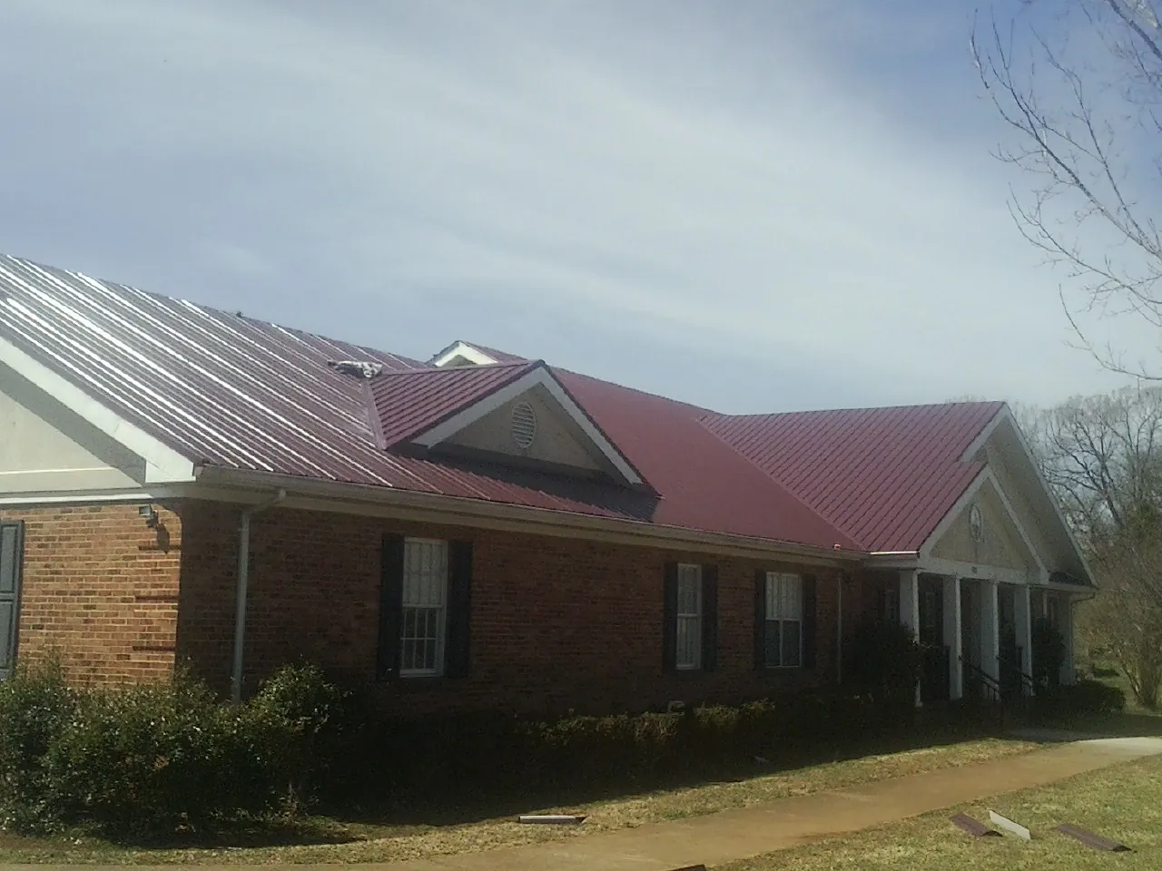 Red metal roof with gabled entries on a long brick building, from a Hail Damage Roof Repair job in Gurley