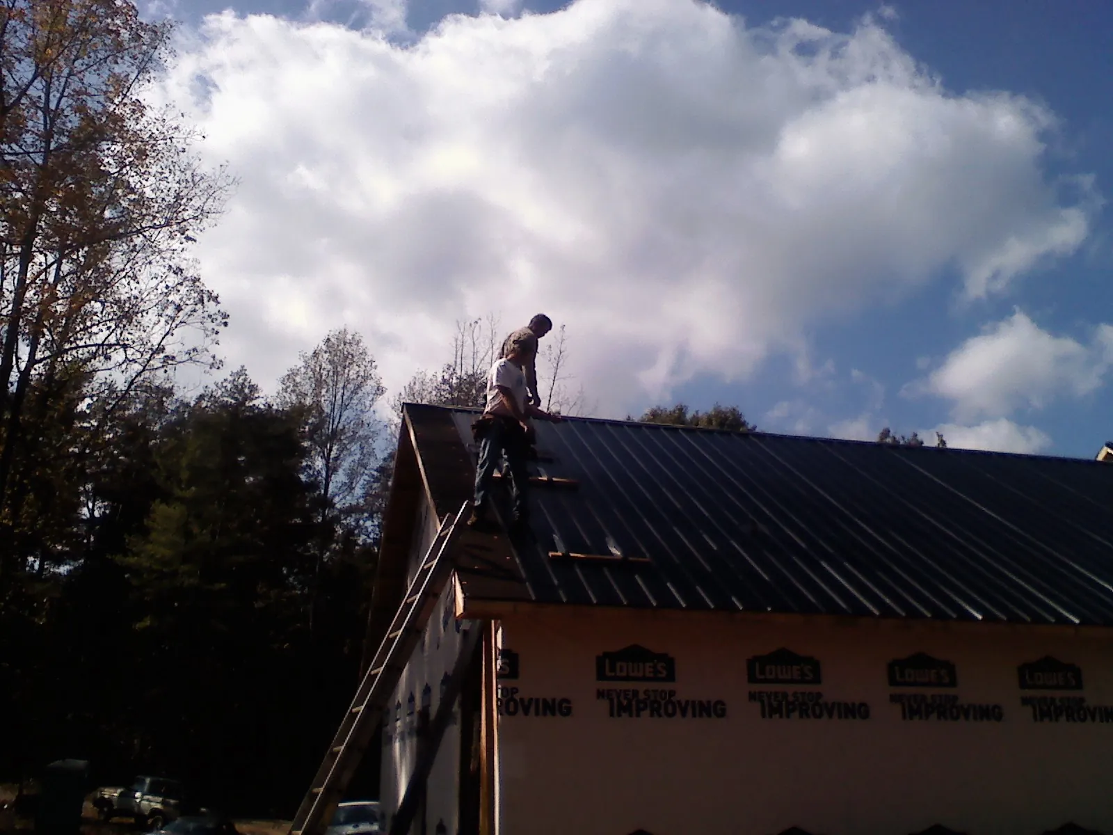 Roofer fastening dark metal panels high against a cloudy sky, from a Roof Inspection job in Gurley