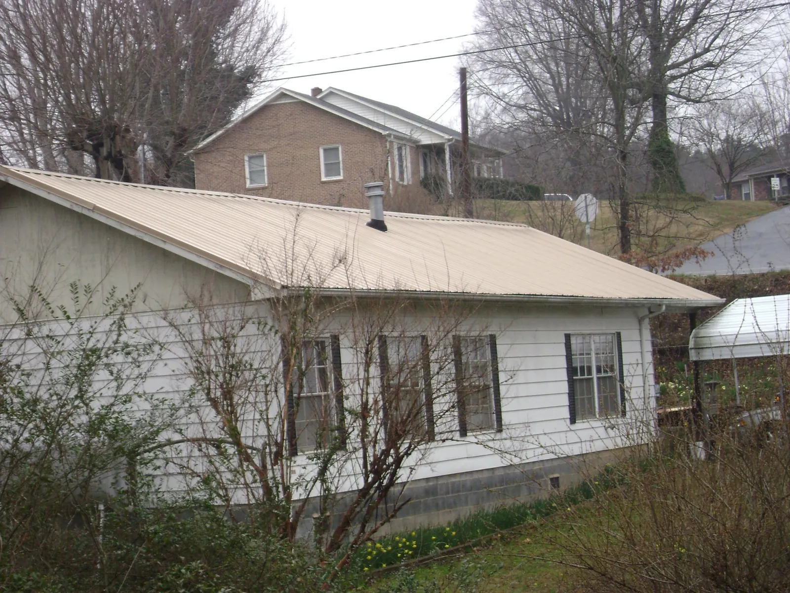 Tan metal roof on a white sided house set into a hillside — Commercial Roofing by Roofing Brothers in Gurley