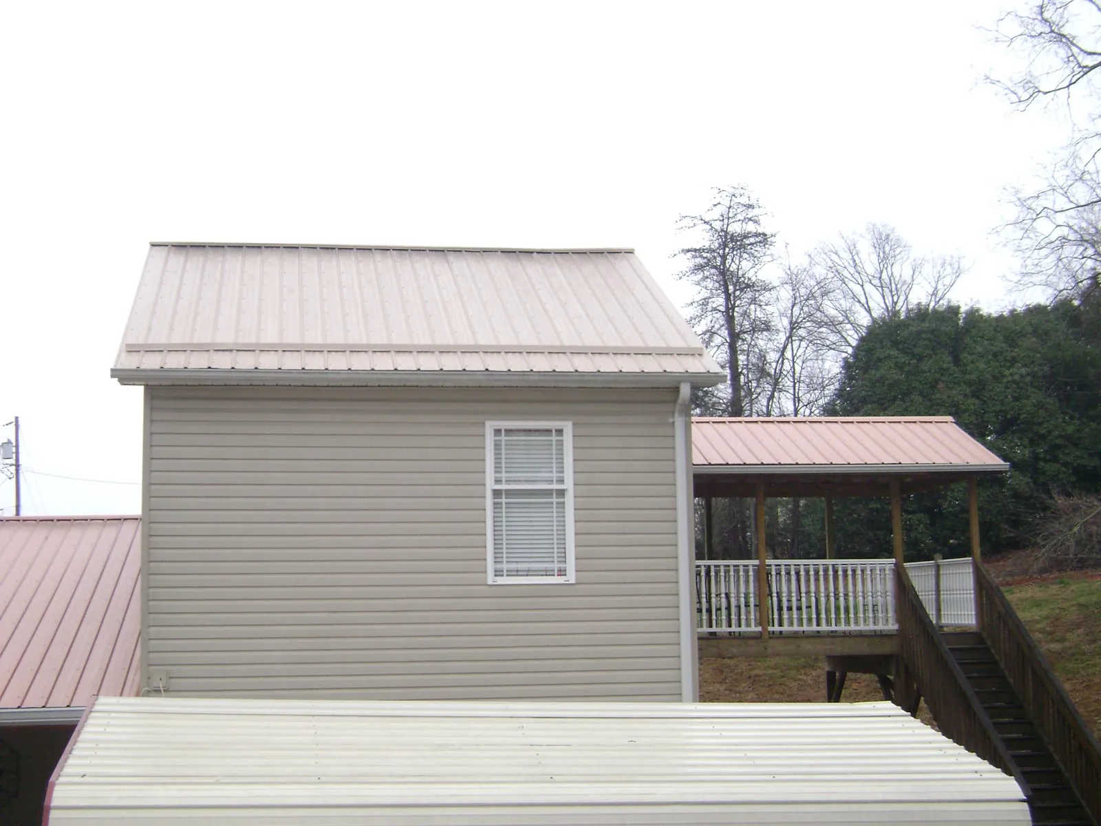 Tan metal roofs on a two story addition and attached porch, from a Roof Replacement job in Gurley